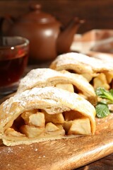 Pieces of tasty apple strudel with powdered sugar and mint on wooden table, closeup