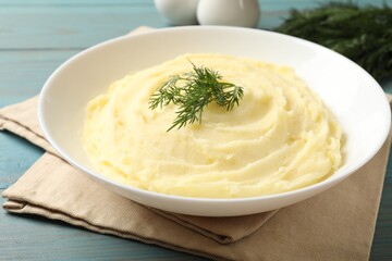 Tasty mashed potato with dill in bowl on light blue wooden table, closeup