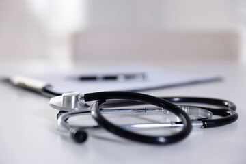 Stethoscope and paperwork on white desk in hospital, selective focus. Space for text