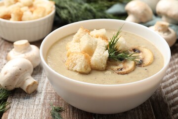 Delicious mushroom cream soup with croutons, dill and ingredients on wooden table, closeup
