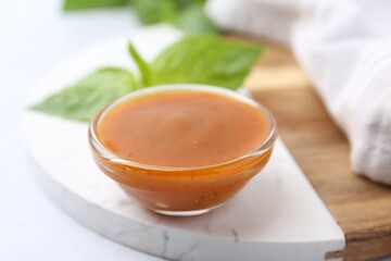 Tasty curry sauce in glass bowl and basil on white table, closeup