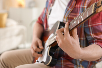 Man playing guitar at home, focus on hand