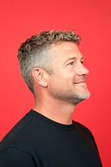 Fototapeta premium Visual idea of style for aging men. Chic men's slick back with fade haircut - midlife white man with blond hair. A classy midlife man with a timeless look. Red solid background.