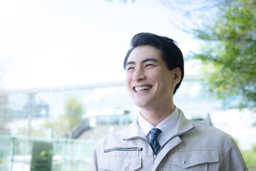 青空のビルの前で作業着を着て笑う爽やかな男性　未来や希望を見つめる正面　施工管理などの作業者のイメージ