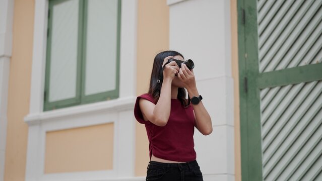 Young Asian woman photographing city architecture with digital camera outdoors, showing creativity, fashion, and lifestyle in an urban setting full of inspiration and focus.