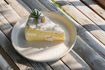 fresh coconut cake decorated with yellow pollen and violet flowers and green leaves on a ceramic plate on bamboo floor background, food, dessert, copy space