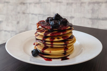 Pancakes with blueberries and fruit syrup stacked on the white plate. A dish with homemade sweet...