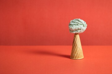 Upside down sugar cone with mint chip ice cream on the top with an orange background