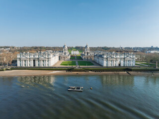 Aerial view of the Old Royal Naval College in Greenwich, London, with twin domed buildings, Thames River, green lawns, and pathways leading to Queen's House. © Aerial Film Studio
