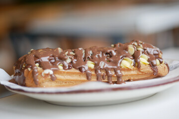 Delicious eclair topped with chocolate and nuts on a plate
