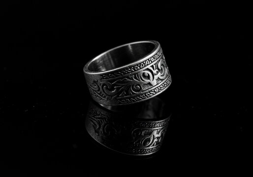 Anel masculino de prata envelhecida com detalhes em relevo e acabamento fosco, fotografado com fundo preto refletivo. Joia de estilo cl&aacute;ssico com pegada contempor&acirc;nea e elegante.