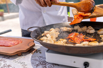 Chef adding dried tomatoes to chicken in paella pan