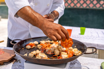 Chef adding chorizo to paella with chicken and vegetables