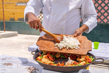 Chef adding chopped onions to paella pan outdoors