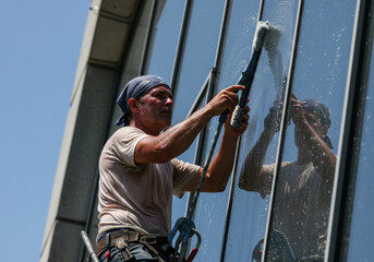Man cleaning window with a window cleaner, tool in hand, focused expression. Skyline visible through clean glass.