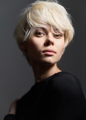 Young woman with short blonde hair posing confidently against a dark backdrop, expressing a sense...