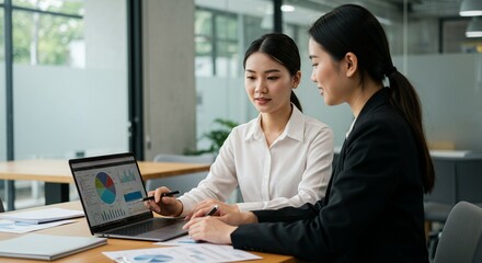Business team meeting in a modern office, discussing data around a table with a laptop.