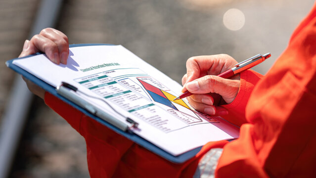 Close-up at safety supervisor's hand during writing on chemical safety checklist to verify the hazardous or risk. Industrial safe work practice concept, selective focus.