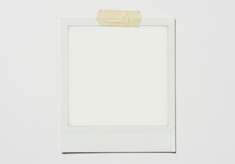 A blank polaroid frame is taped to a white wall creating a minimalist and clean aesthetic look