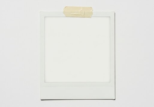 A blank polaroid frame is taped to a white wall creating a minimalist and clean aesthetic look