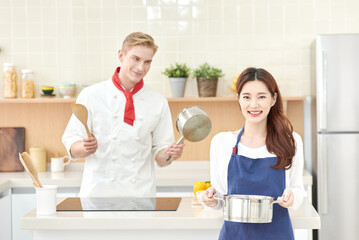 Beautiful Asian Woman in Apron and Caucasian Male Chef Cooking Together in Modern Kitchen