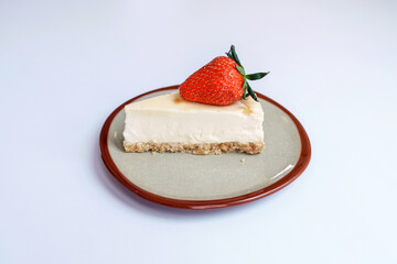 Homemade dessert bakery cafe. Sliced classical plain New York cheesecake with fresh strawberry in vintage style ceramic plate on table with white background.