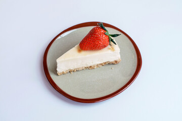Homemade dessert bakery cafe. Sliced classical plain New York cheesecake with fresh strawberry in vintage style ceramic plate on table with white background.