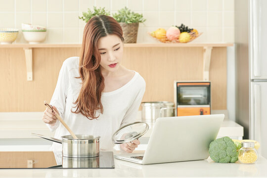 Young Woman Cooking with Laptop in Bright Kitchen