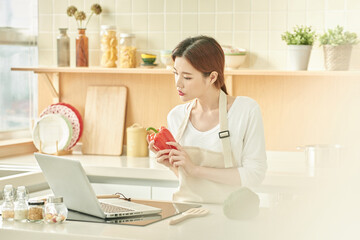 Young Woman Holding Bell Pepper and Using Laptop in Modern Kitchen