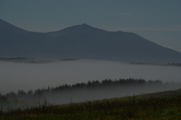 夜霧で霞む北海道美瑛の丘陵地帯と星空