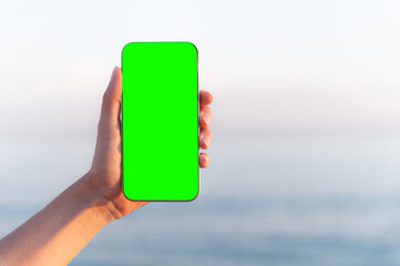 GREEN SCREEN CHROMA KEY A female person interacts with a smartphone on a beach with a green screen,...