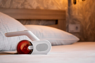 Housewife vacuuming white pillows on bed with handheld vacuum cleaner, close-up