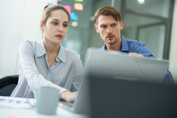 Collaborative business meeting between two professionals in an office setting discussing project details with a laptop