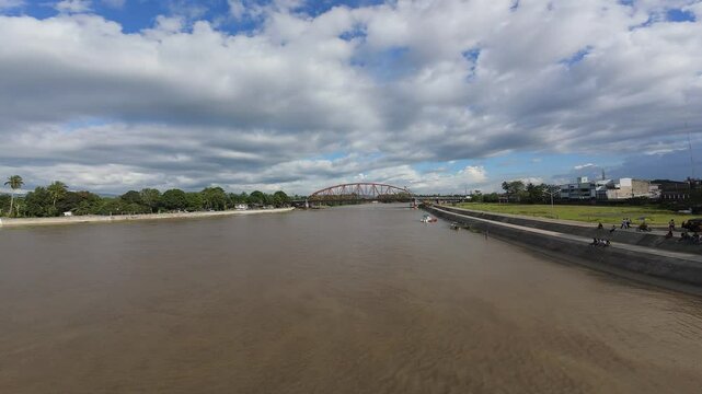 A low-angle FPV flight travels from Butuan toward CDO, gliding over the brown waters of the Agusan River and the red iron Magsaysay Bridge in Mindanao, Philippines.
