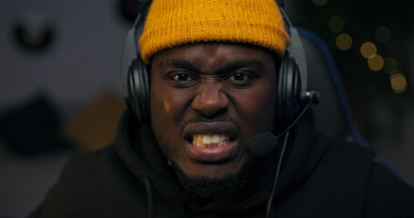 A focused gamer sits in a dark LED-lit room, staring at the screen in shock. He wears a headset and talks to his online team, planning a strategy after a surprising game twist.