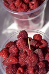 Red raspberries in large plastic cups. Sale of fresh ripe juicy berries, street trade. Healthy and...