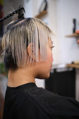 Fototapeta premium Hairdresser cutting wet hair of young female model in salon