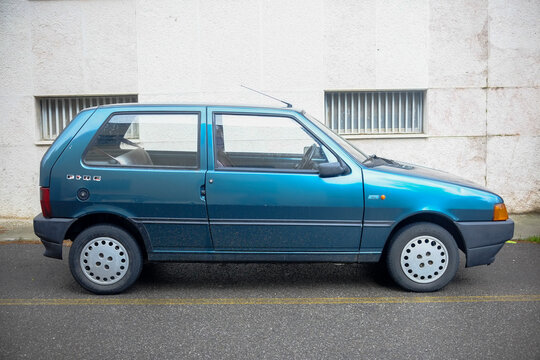 Vintage turquoise Fiat Uno 1.0 Fire, first generation, resting beside urban street wall, showcasing late 1980s automotive design