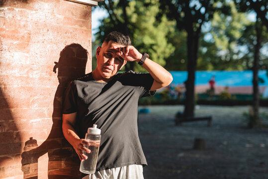 Middle aged Southeast Asian man wipes sweat from his brow, exhausted after exercising in hot and humid weather at the park.