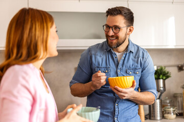 A happy couple enjoys breakfast in their cozy kitchen, laughing as they prepare cereal. Their warm and loving interaction reflects a strong relationship and a joyful morning routine.