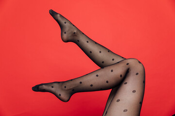 Slender female legs in black stockings, tights on a red background