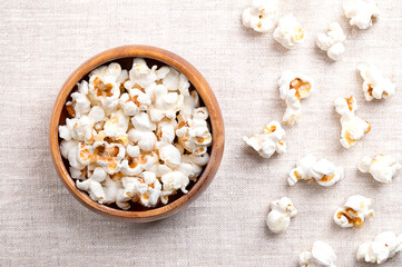 Popcorn, popped corn in a wooden bowl on linen fabric. Seeds of the Zea mays variety everta, expanded and puffed up, after heated. Snack food, also called popcorns and pop-corn.