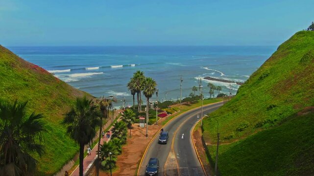 Curved coastal road with cars, green hills, and ocean view in Miraflores, Lima, Peru