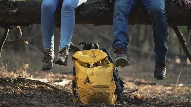 Cinematic shot. Tourists rest on log travel break with backpack. Journey pause travelers boots dangle. Nature respite for tourists travel tranquility. Forest travel tourists moment of repose.