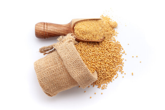 A scoop of organic Yellow Mustard seeds (Sinapis alba) powder, along with whole mustard seeds spilled out from a jute bag. Isolated on a white background.