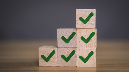 Wooden blocks stacked in a pyramid shape, each featuring a green check mark, symbolizing...