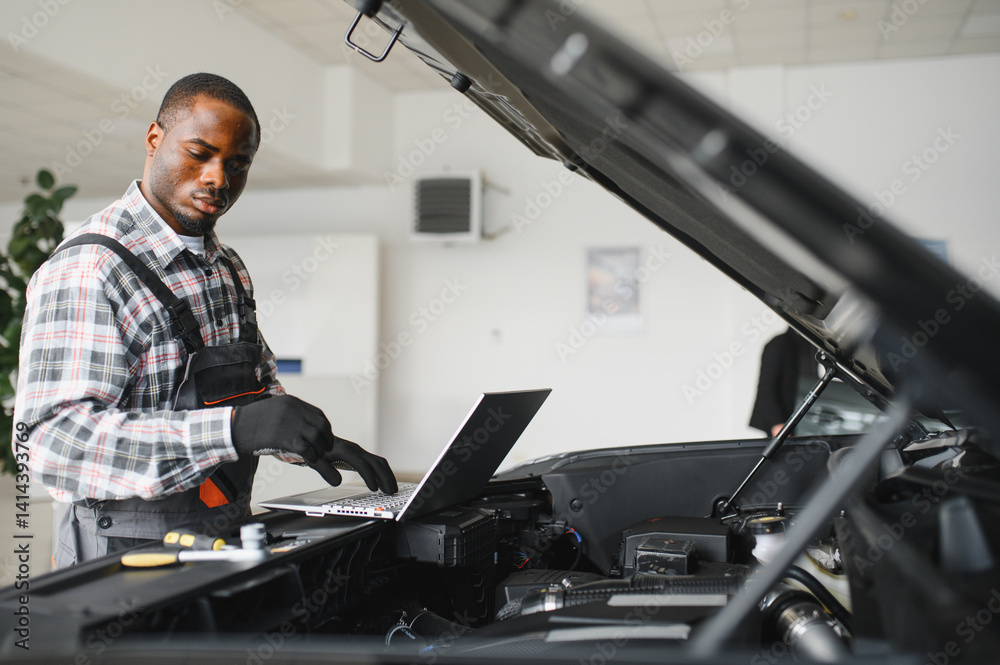 Poster Black auto mechanic running diagnostic on laptop while analyzing engine problems in a workshop