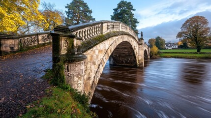 Fototapeta premium Autumnal stone arch bridge over river, parkland background