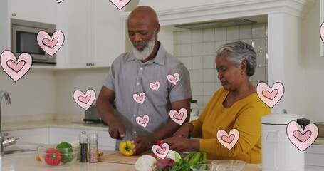 Image of pink hearts over happy african american senior couple preparing food in kitchen
