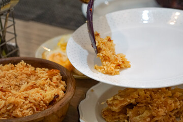 A person serving a portion of delicious fried rice from a wooden bowl onto a plate. The scene captures a culinary moment at a dining table, showcasing freshly prepared food and appetizing details.